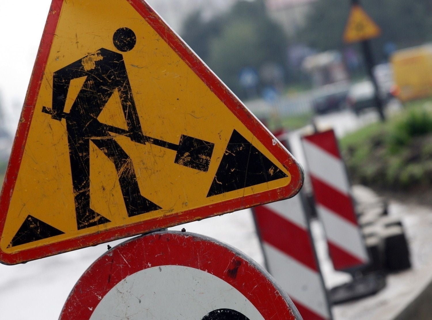 Zdjęcie znaku drogowego oznaczającego roboty drogowe, w tle rozmyte kształty innej infrastruktury drogowej.