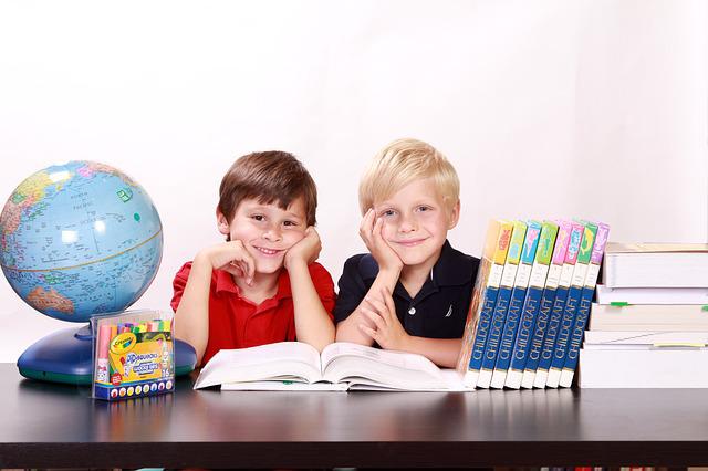 Dwóch chłopców w wieku szkolnym. Na stole znajduje się globus i książki, fot. pixabay