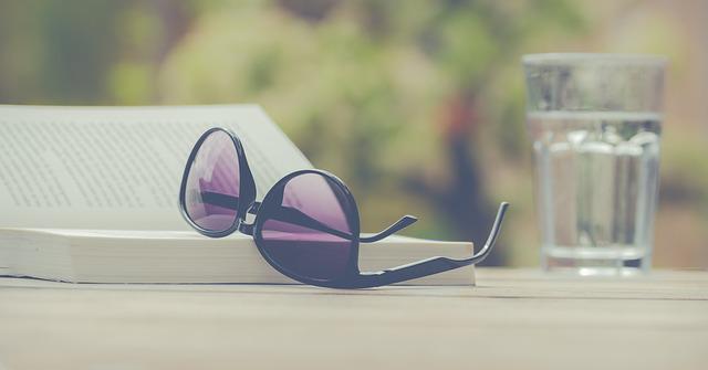 Na stoliku umieszczono okulary przeciwsłoneczne, książkę i szklankę wody, fot. pixabay