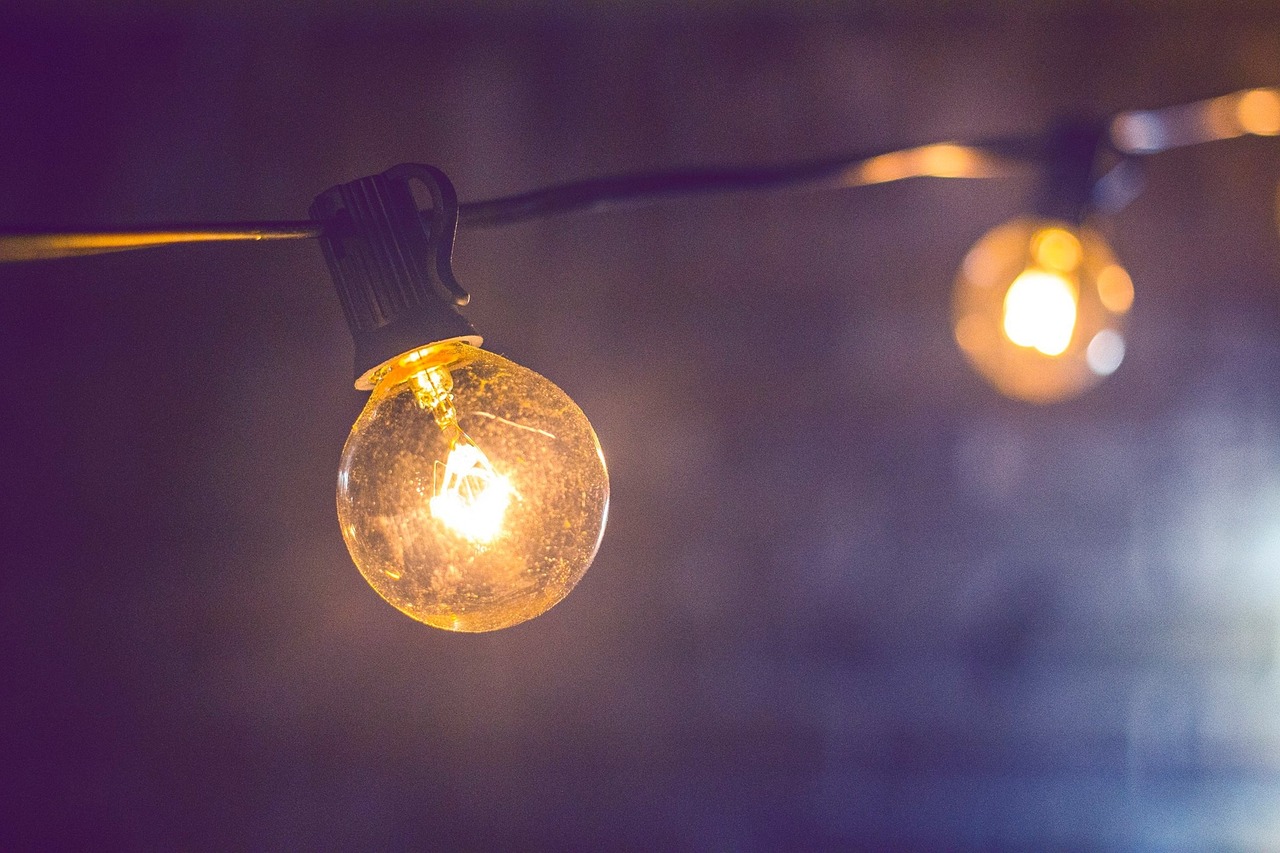 Dwie ozdobne żarówki na fioletowym tle, wiszące na kablu; zdjęcie przykładowe, fot. Pixabay