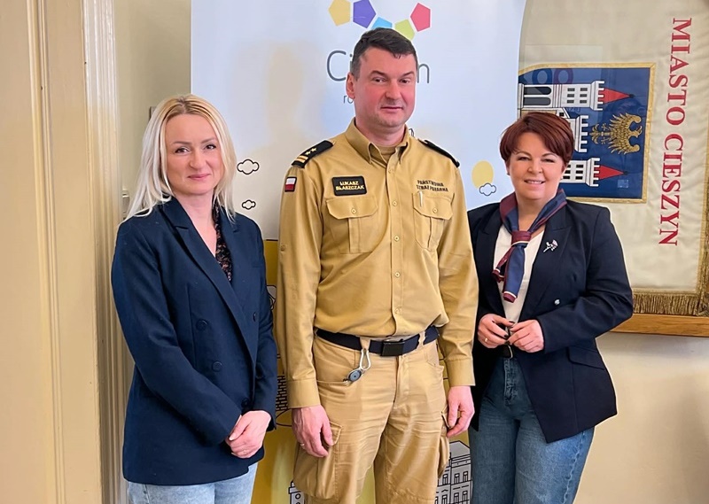 Zdjęcie przedstawia trzy osoby stojące obok siebie w przestrzeni urzędowej. W tle widoczny napis „Miasto Cieszyn”.