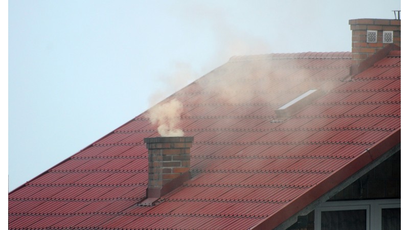 Zdjęcie przedstawia czerwony dach na budynku. Na dachu znajduje się komin, z którego wydobywa się dym. Zdjęcie: Pixabay