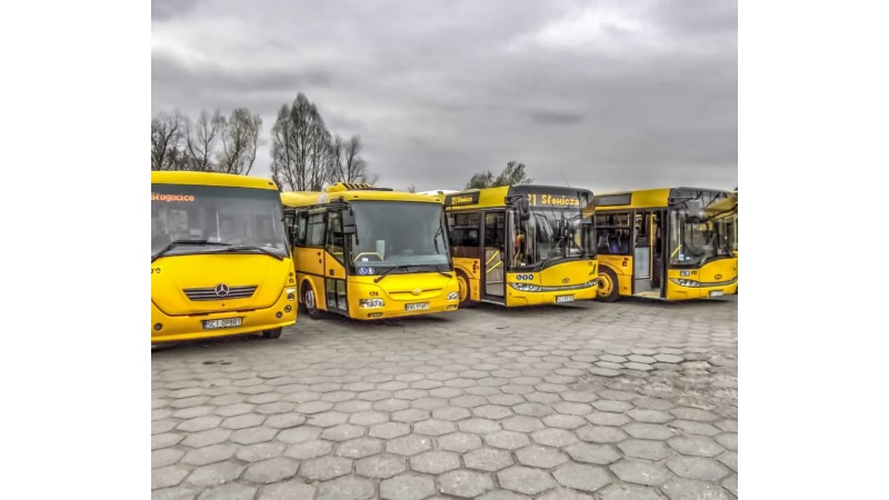 Zdjęcie przedstawia cztery autobusy cieszyńskiej komunikacji miejskiej w kolorze żółtym. Pojazdy stoją na parkingu wyłożonym szarą kostką brukową.