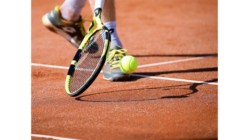 Zdjęcie przestawia buty sportowca, kawałek kortu i rakietę tenisową. fot. pixabay