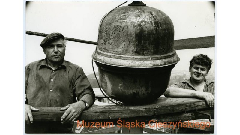 Czarno-białe zdjęcie przedstawiające dwóch mężczyzn pracujących przy remoncie wieży ratuszowej w 1984 r., a także montowaną wówczas banię. Zdjęcie autorstwa Tadeusza Popiela, z zasobów Muzeum Śląska Cieszyńskiego.