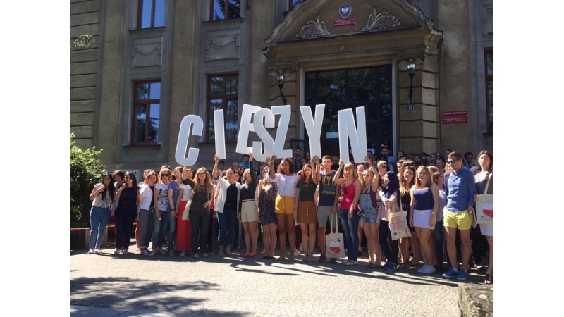 Uczestnuicy Letniej Szkoły przed budynkiem filii Uniwersytetu Śląskiego, trzymający w rękach duże białe litery układające się w napis 